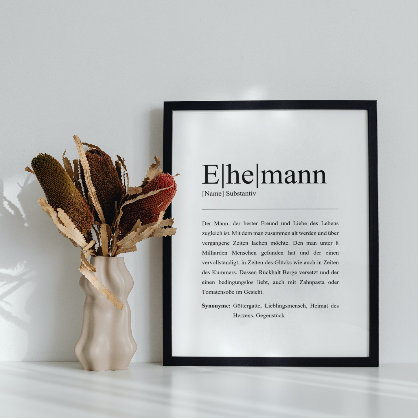 Ehemann Poster in schwarzem Rahmen in modernem Wohnzimmer. Dekoriert mit stilvollem Trockenblumenstrauß in unikater Vase. Zeitloses, personalisierbares Dekor für jeden Wohnraum, perfekt für Liebhaber kreativer Geschenke.