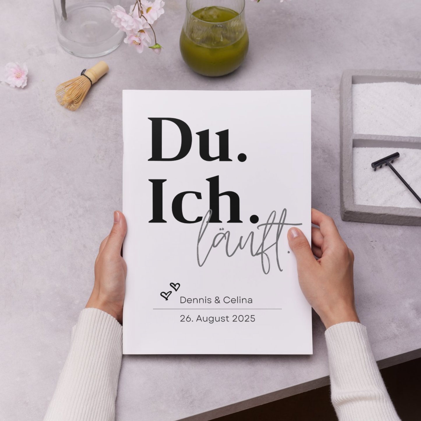 Hände halten das minimalistische personalisierte Poster Du Ich läuft mit den Namen Dennis und Celina und Datum 26 August 2025. Geeignet für einzigartige Geschenke und Paare.