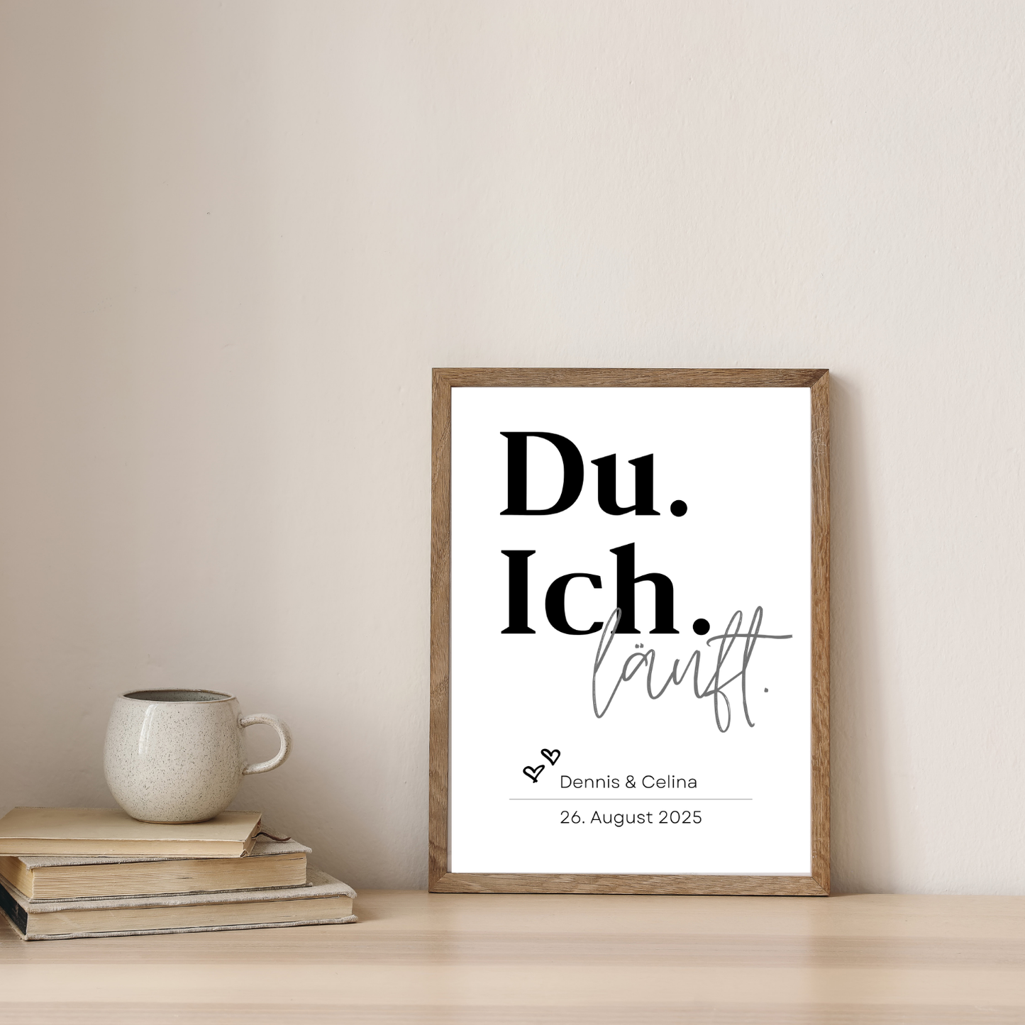 Stilvolles personalisiertes Poster Du Ich läuft in einem Holzrahmen. Dekoriert auf einem Tisch neben Büchern und einer Tasse. Perfekt für Hochzeit oder Geschenk zum Jahrestag mit den Namen Dennis und Celina.