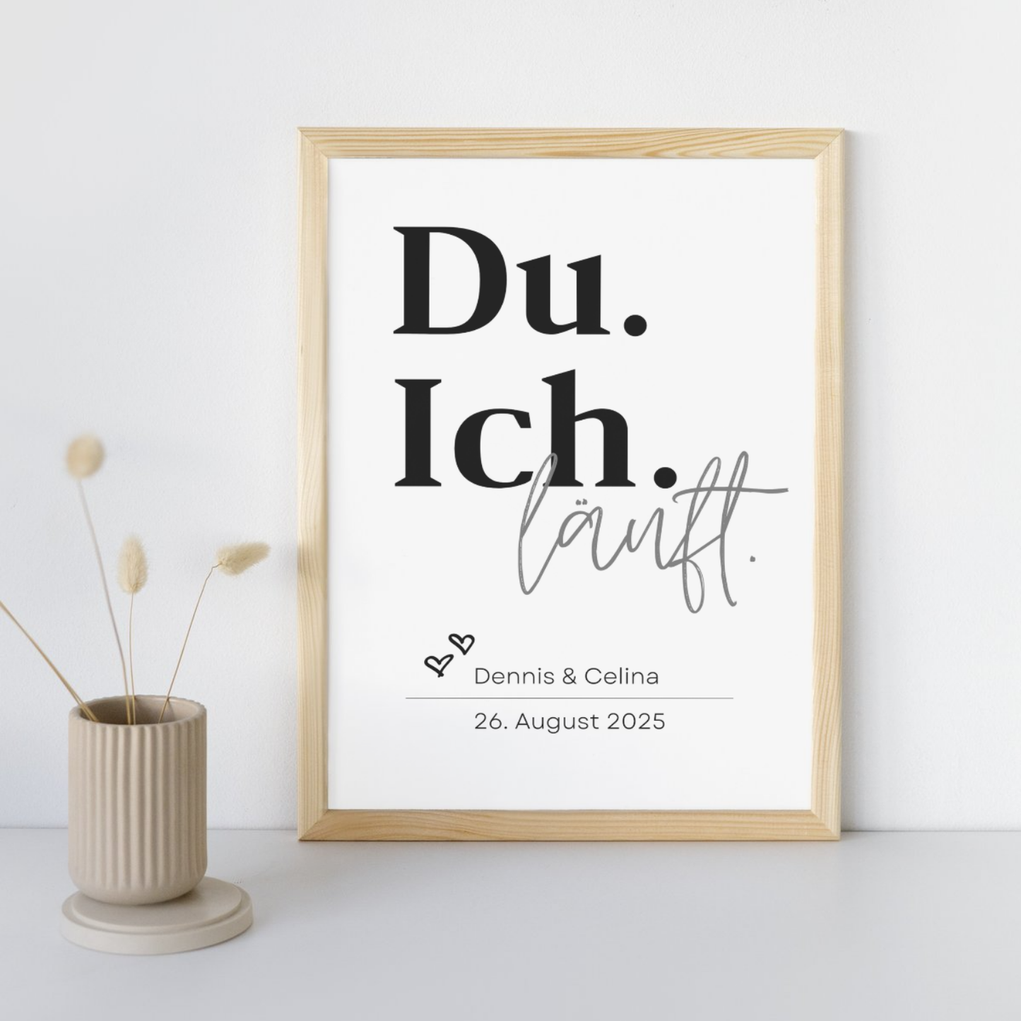Minimalistisches Poster mit dem Spruch Du Ich läuft in einem Holzrahmen. Personalisiert mit den Namen Dennis und Celina und Datum 26 August 2025. Perfektes Geschenk für Paare und Hochzeiten modern dekoriert mit einer Vase.