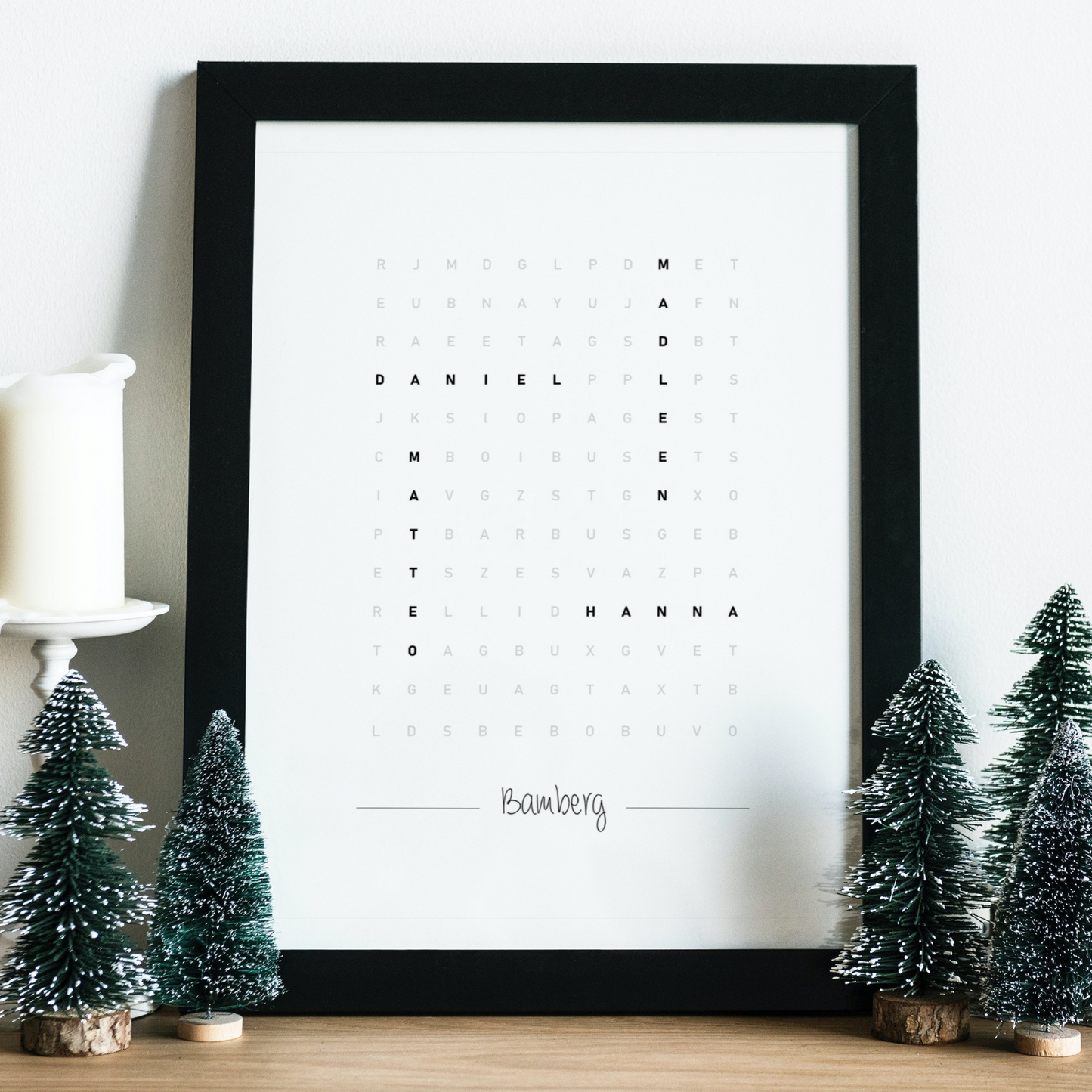 Skandinavisch inspirierte Wanddekoration. Gerahmtes Poster im Wortsuche-Stil platziert zwischen Tannenbaum-Kerzen. Ideal zur Ergänzung von Weihnachtsdekorationen in schlichtem Raumdesign.
